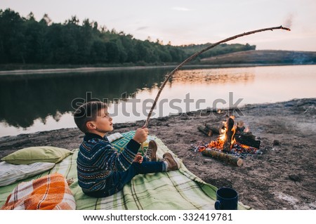 Little boy cooking a marshmallow over a campfire at night