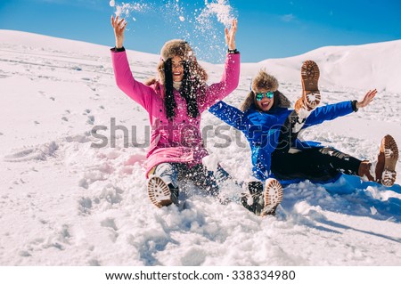 Two girlfriends have fun and enjoy the fresh snow on a beautiful winter day in the mountains