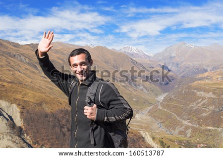 Happy tourist traveler with a black backpack in the mountains, smiling welcomes hand