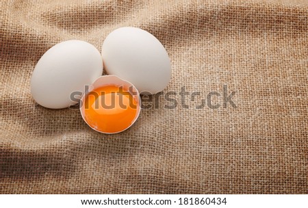 two whole and one broken egg with yolk on burlap background