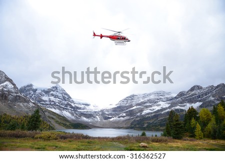 red helicopter taking off near snow mountain in alberta, canada