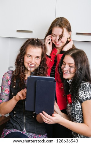 Three women friends chatting at home and using laptop to look at new photo or browsing internet for information