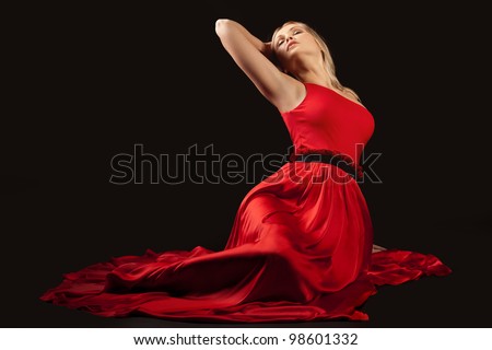 Beautiful girl in long red dress sitting on floor. Black background.