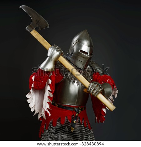 Powerful knight in the armor. Medieval knight in the field with an axe. Dark background.