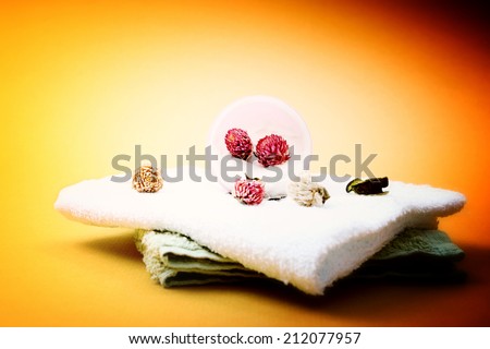Spa essentials (cream, white towel and pink flowers) isolated on yellow