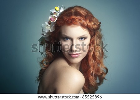 Young beautiful red haired woman smiling with an orchid in her hair, bright blue background