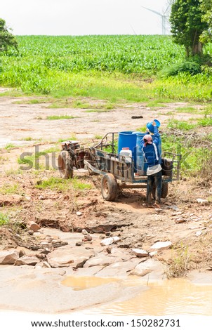 A man carry a pail water to the old truck in the nature field