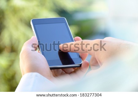Over the shoulder view of young man using a mobile smart phone outdoor, blurred background