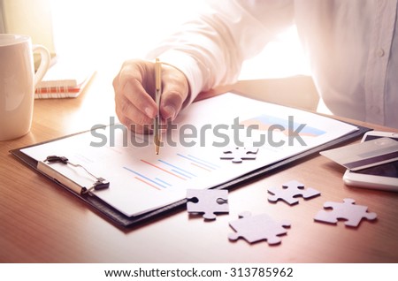 Businessman work with financial report at wooden office desk with puzzle pieces, smartphone, credit card and coffee cup. Concept for business, finance, marketing.