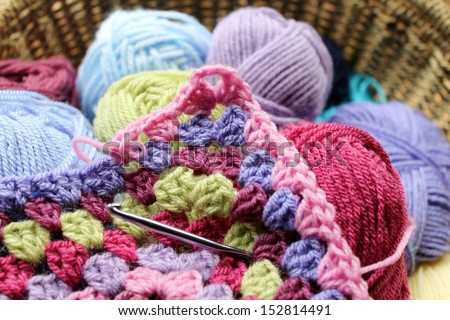 Crochet, the making of a crocheted wool afghan blanket, a retro craft. In a basket with balls of yarn, colors are green, pink, blue and purple