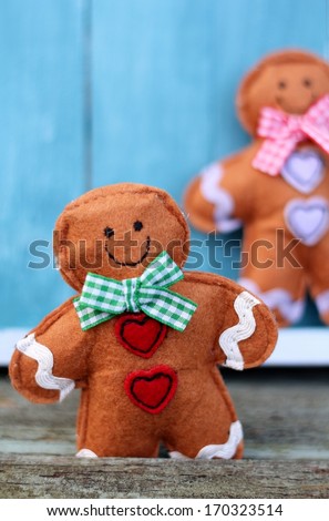 Cute felt toy shabby chic gingerbread man on painted blue wooden boards, fairy tale character wearing  a smile, gingham bow and heart buttons, valentine or christmas decoration