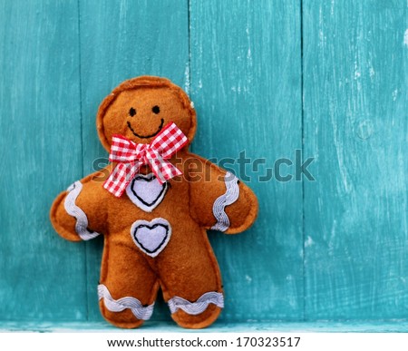 Cute felt toy shabby chic gingerbread man on painted blue wooden boards, fairy tale character wearing  a smile, gingham bow and heart buttons, valentine or christmas decoration