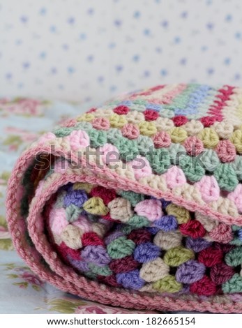 Folded crochet afghan blanket in shabby chic bedroom, granny stitch in yarn of pink, cream, pink, purple and cream