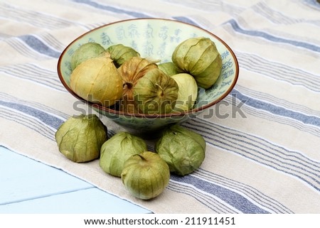 Ceramic bowl of green Tomatillos in their paper like outer skin, laying on blue striped cotton cloth towel, napkin