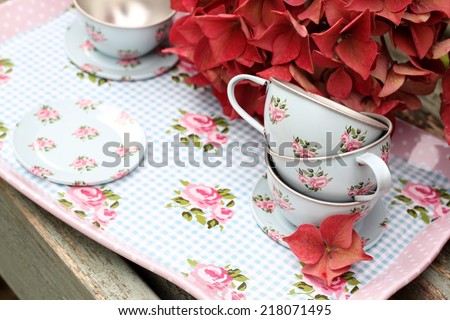 Toy duck egg blue tin cup and saucers on a tray  on weathered wooden bench, with autumn faded pink hydrangea flowers, shabby chic, vintage image