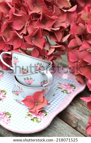 Toy duck egg blue tin cup and saucers on a tray  on weathered wooden bench, with autumn faded pink hydrangea flowers, shabby chic, vintage image