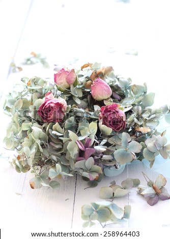 Over exposed, pale image of dried blue hydrangea and pink rose buds, a romantic, ethereal flower arrangement on white wooden floorboards, wedding bouquet in pastel colors  shabby chic