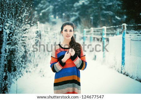 Outdoor portrait of young beautiful brunette posing outdoor in winter park. Girl dressed in color sweater.