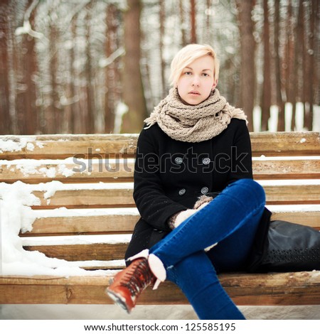 Young beautiful blonde girl sitting on the bench in winter park