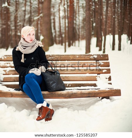 Young beautiful girl sitting on the bench in winter forest
