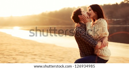 Young attractive couple in love kissing on the beach in evening. Cold weather, soft sunny colors.