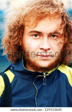 Outdoor portrait of young handsome smiling ginger curly man with beard