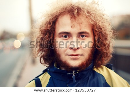 Outdoor portrait of young handsome smiling ginger curly man with beard