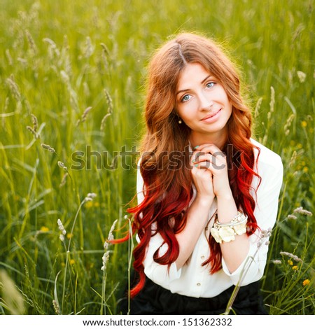 Young pretty ginger sensual smiling woman posing on green field in summer. Cute smiling girl.