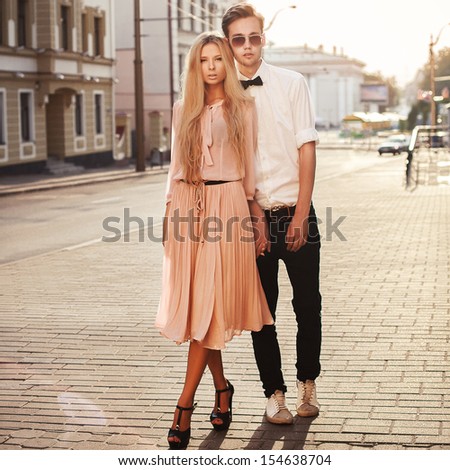 Young Fashion Elegant Stylish Couple Posing On Streets Of European City In Summer Evening Weather. Sensual Blonde Vogue Girl With Handsome Hipster Man Having Fun Outdoor.