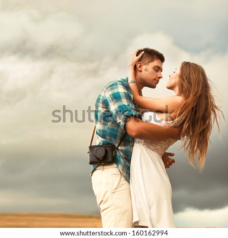Stunning sensual outdoor portrait of young stylish fashion couple posing in summer in corn field behind rainy clouds and storm.