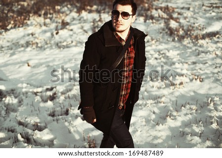 young handsome man posing outdoor in snow field in winter outdoor alone. Smiling well dressed and fashion style cold portrait
