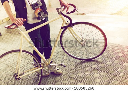 Young handsome stylish hipster man posing on the street with vintage camera and bike on the street in sunny summer day