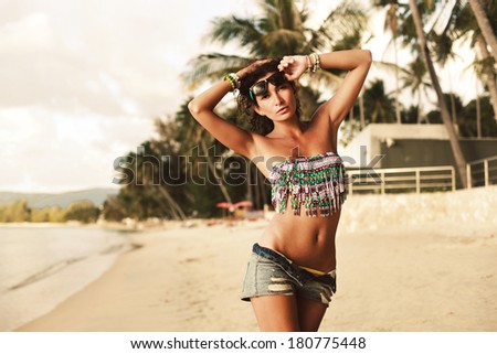 Outdoor fashion warm colors portrait of young sensual happy woman in jeans shorts and bikini posing on the beach in tropic country
