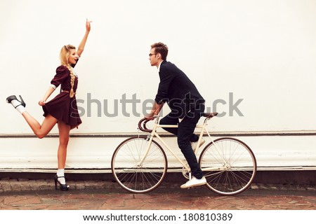 Young vintage hipster pretty couple having fun outdoor in summer on the street in city with cool bicycle behind white wall. Man with girl in spring urban style