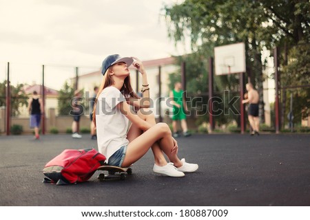 Outdoor fashion portrait of pretty young brunette girl with skateboard on sport basketball school backyard