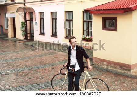 Young handsome man posing on the street in center of town with vintage bike dressed in stylish clothes and having fun outdoor
