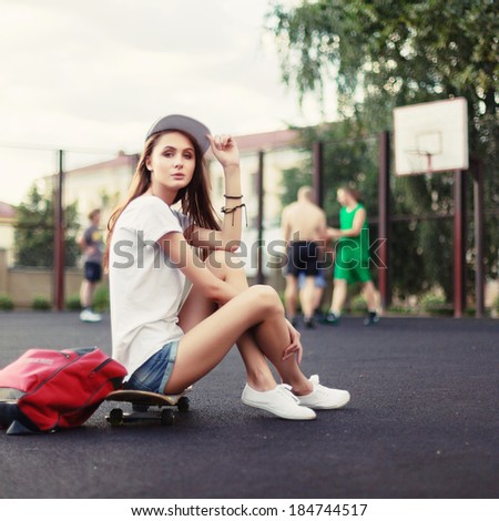 Outdoor fashion stylish portrait of pretty brunette girl posing outdoor in summer with skateboard and backpack traveling urban style