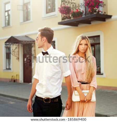 Portrait of pretty young fashion couple posing in summer on the street in city european country together. Hipster style beautiful girl with her handsome man walking outdoor and having fun.