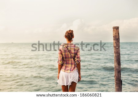 Young pretty woman standing alone on the pier near the sea and looking on the water and waiting for somebody in ocean