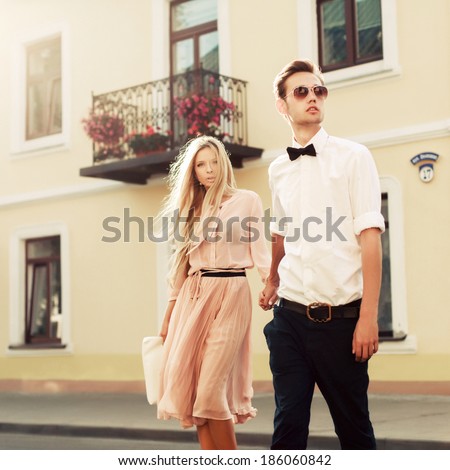 Portrait of pretty young fashion couple posing in summer on the street in city european country together. Hipster style beautiful girl with her handsome man walking outdoor and having fun.