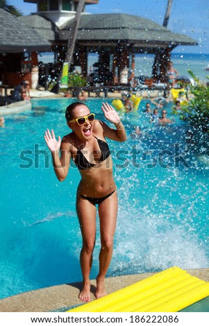 young pretty funny laughing and screaming girl posing on the pool in summer on tropic island because of water splashing