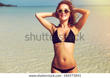 Portrait of pretty beautiful sport fashion woman in black bikini posing in summer near the sea and blue sky in sunshine with gorgeous smile in happy mood on tropic island on vacation