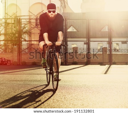 Young hipster man with beard on fixed gear bicycle riding in summer outdoor on the street in city in sunglasses