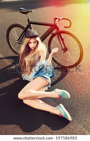 Young pretty fashion woman sitting on the ground with amazing black fixed gear bike in sport style in summer and having fun. Colorful hipster photo