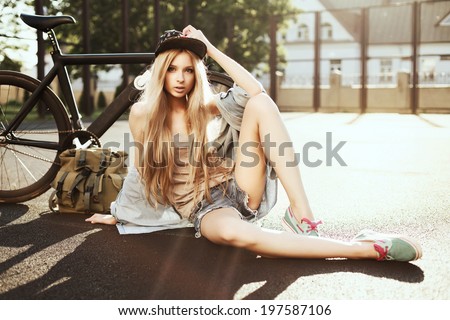 Young pretty fashion blonde woman sitting on the ground with amazing black fixed gear bike in sport style in summer and having fun. vintage hipster photo
