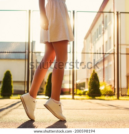 Pretty young sexy sport style woman standing alone in summer evening on the street in sunshine bright light and having fun outdoor