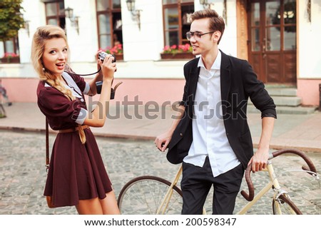 Pretty young blonde vintage style woman making photo oh her handsome hipster boyfriend on the street laughing and having fun in summer