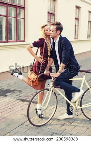 Outdoor fashion vintage portrait of pretty young couple in love with old bicycle and girl giving kiss to her handsome boyfriend on the street
