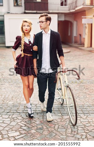Couple in love pretty young blond woman having fun with her handsome hipster style boyfriend walking on the street with vintage bicycle retro style
