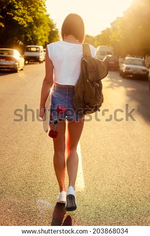 Young sexy fashion sensual woman walking on the street in summer warm evening carrying back pack and moving to sunset hipster style
